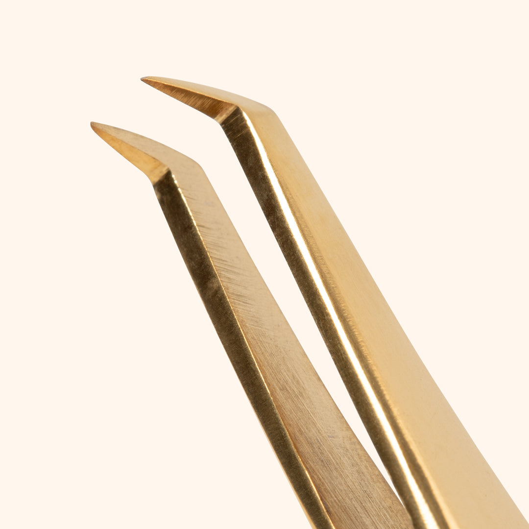 close up to curved thin tip of volume professional tweezers in gold colour 